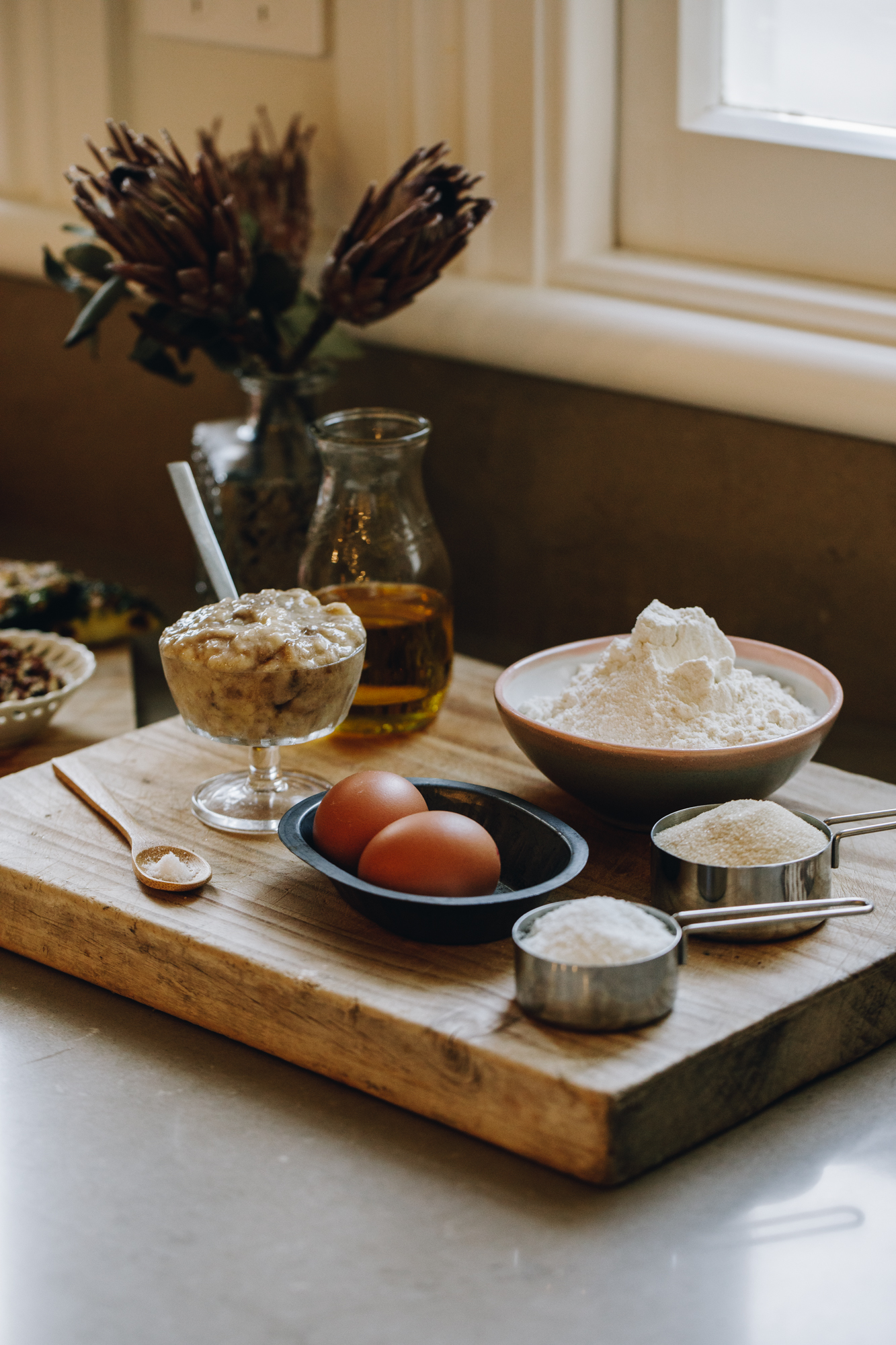 Muffin ingredients on a wooden board with dried flowers in the background, on a stone bench. 