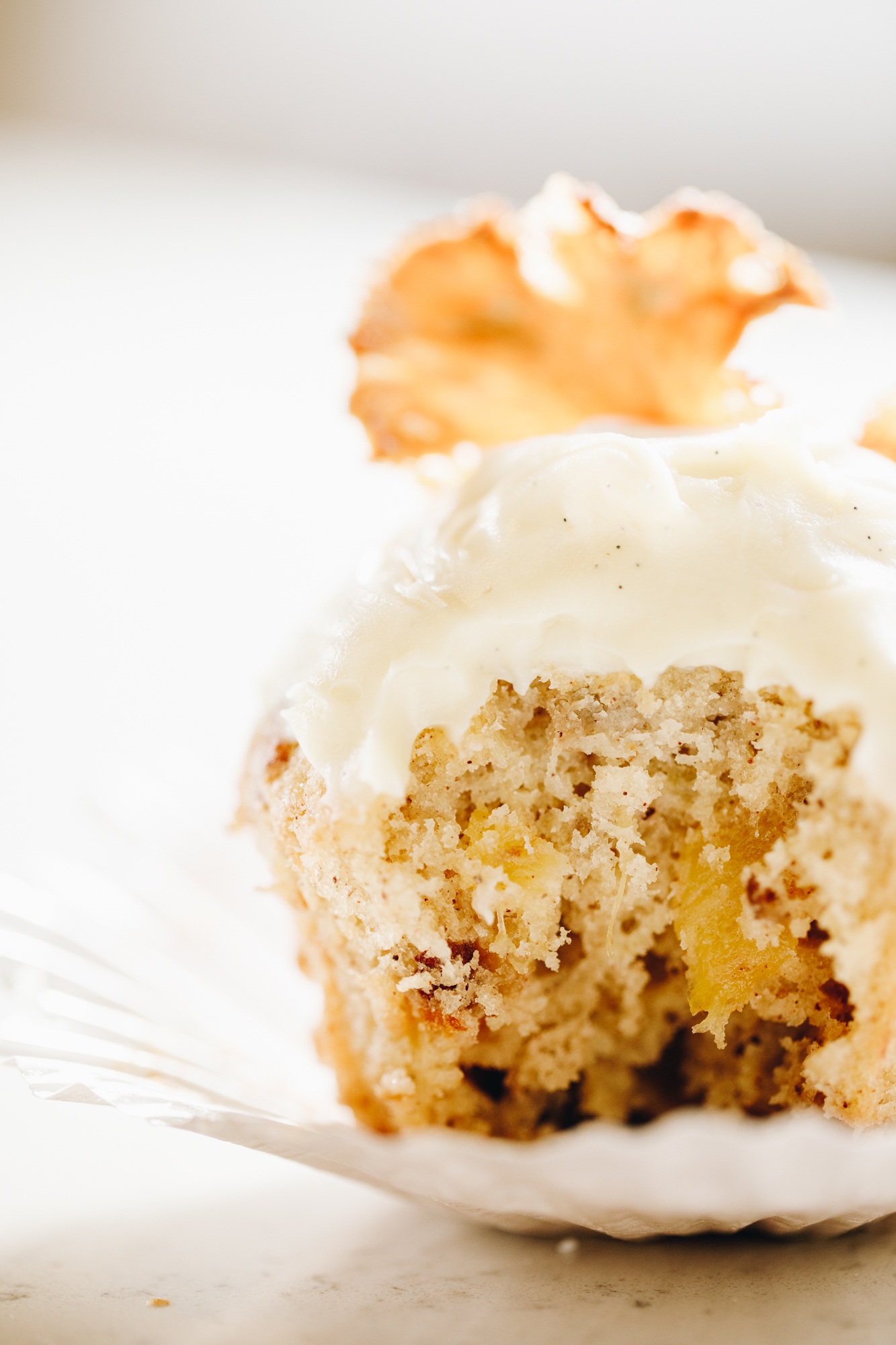 A bitten hummingbird muffin on a muffin case, topped with cream cheese frosting and a pineapple flower. 