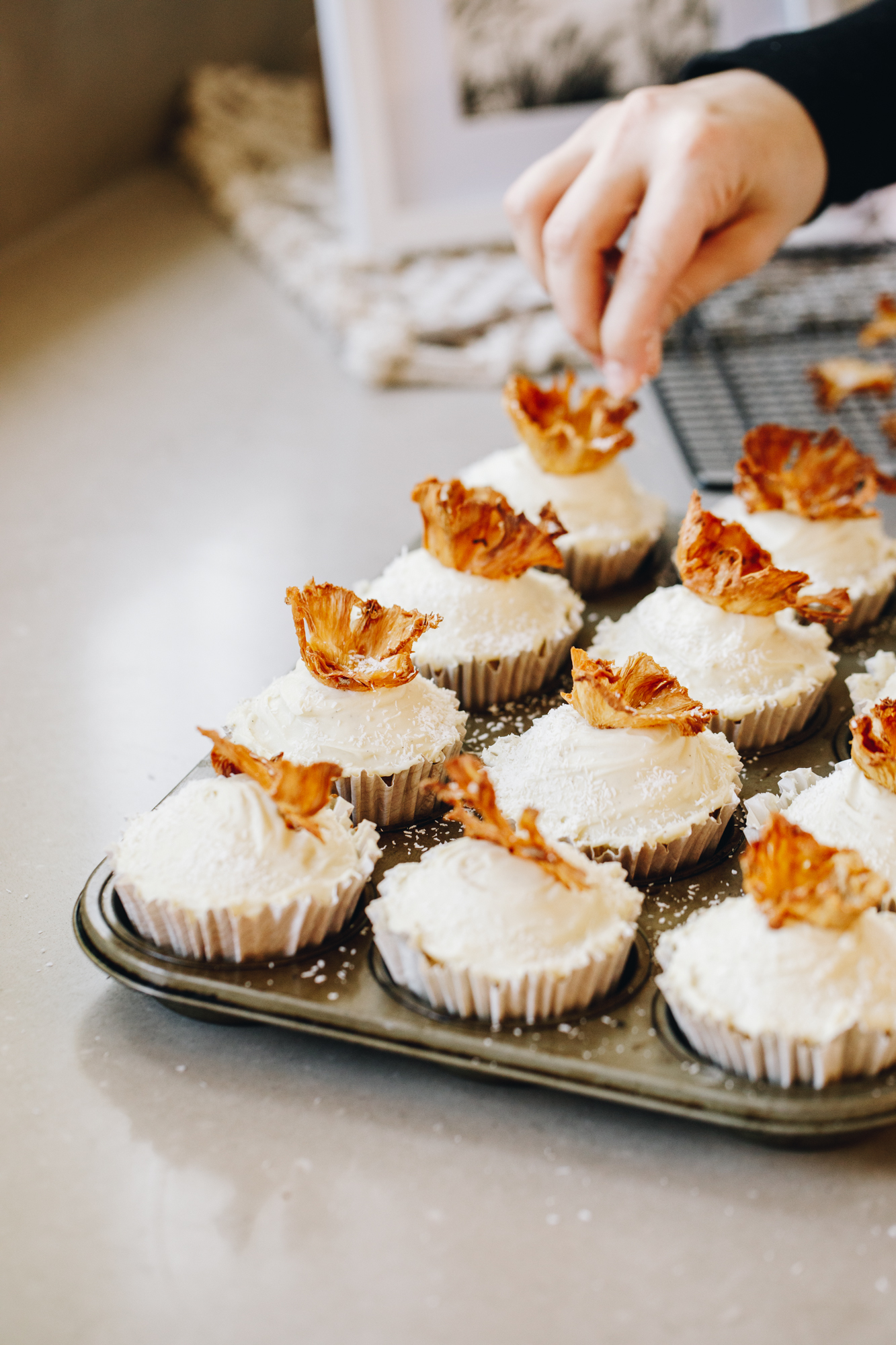 Pineapple flowers are topped on cupcakes, in a muffin tray on a stone bench.