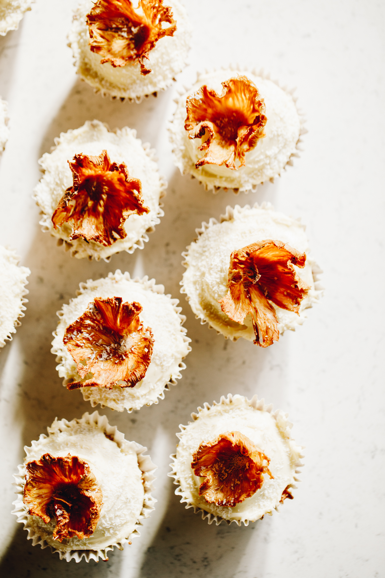 Pineapple flowers on top of cupcakes with white icing, on a white bench.