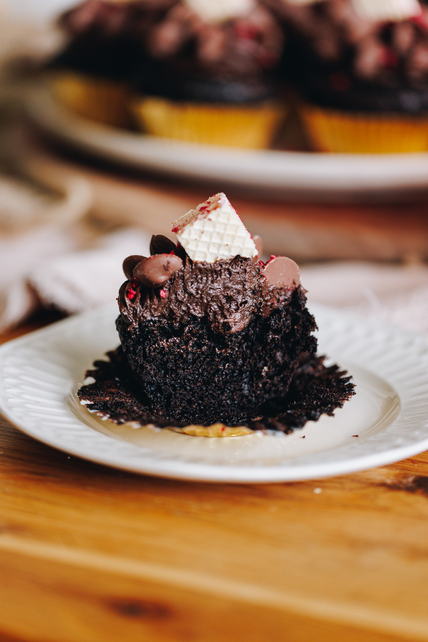 A double chocolate muffin sliced open with buttercream on top, on a plate, on a wooden table. 