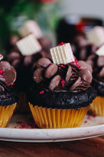 Decorated double chocolate muffins, in gold cupcake cases, on a pink plate, on a wooden board.