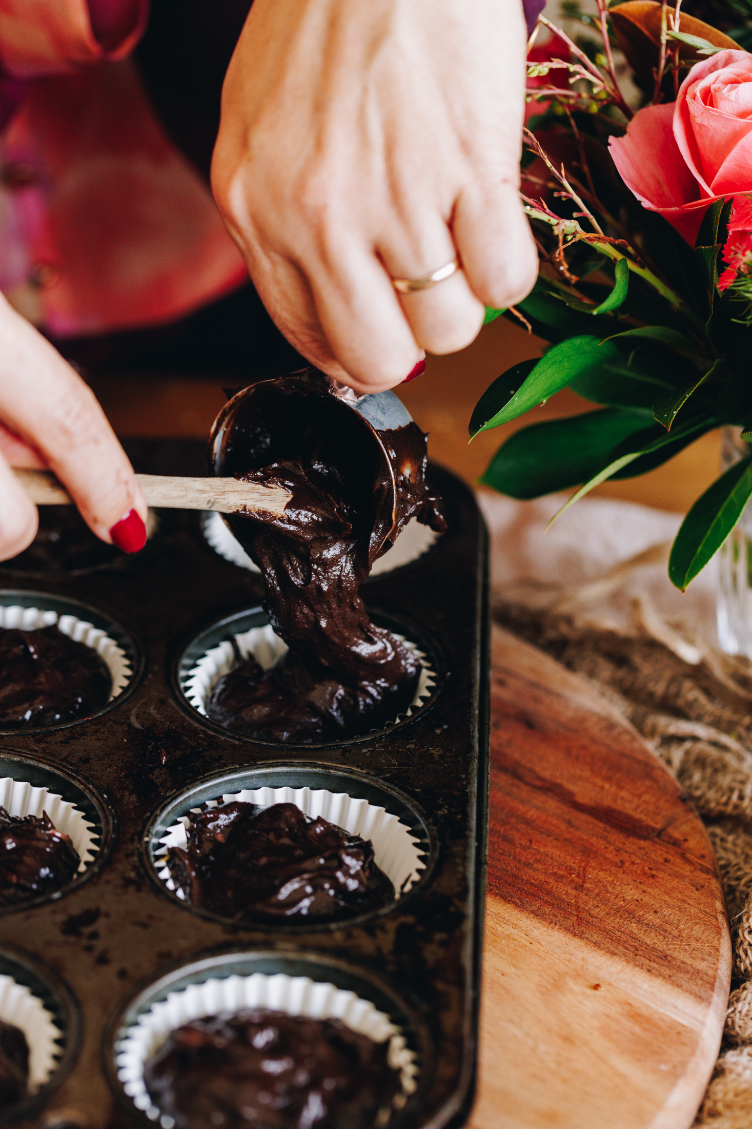 Muffin batter being added to cupcake cases in a muffin tray. 