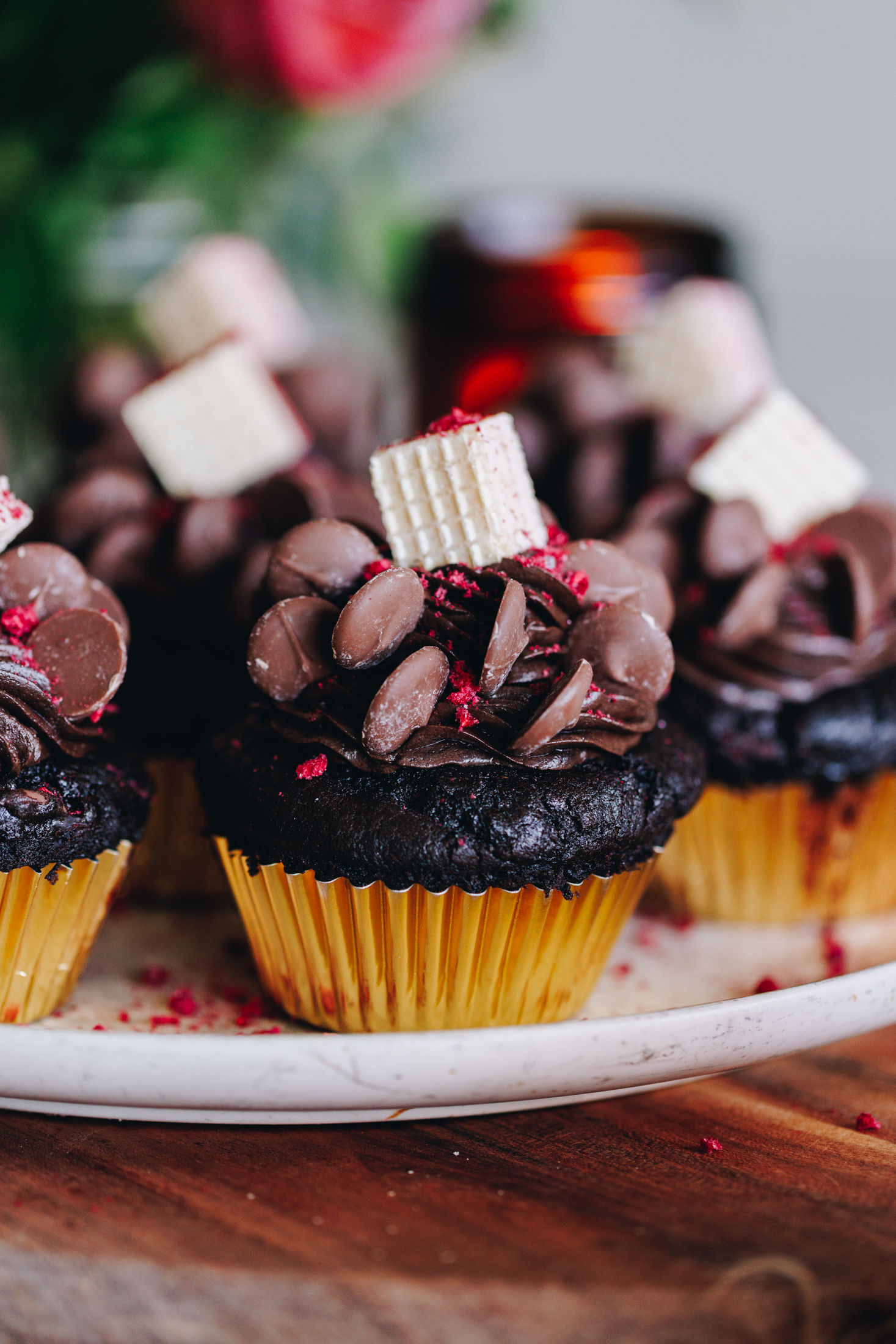 Decorated double chocolate muffins, in gold cupcake cases, on a pink plate, on a wooden board.