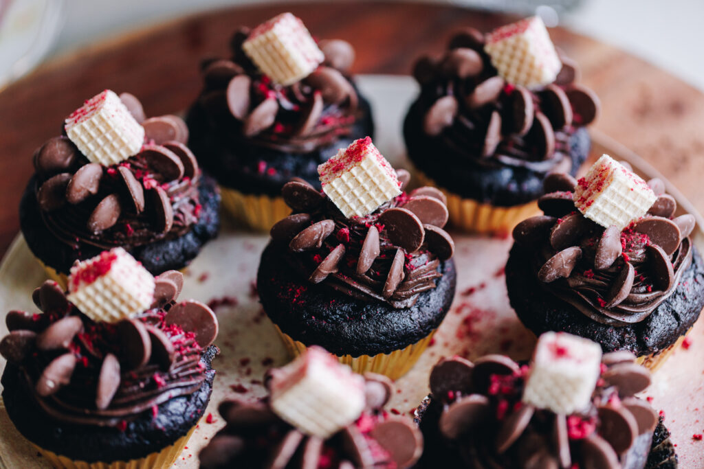 Decorated double chocolate muffins, in gold cupcake cases, on a pink plate, on a wooden board.