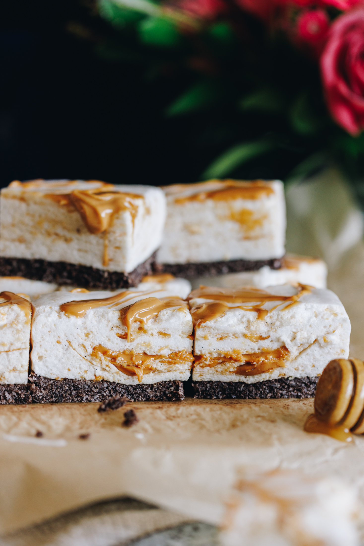 No-bake peanut butter marshmallow slice stacked on baking paper, flowers in the background. 