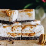 No-bake peanut butter marshmallow slice stacked on baking paper, flowers in the background.