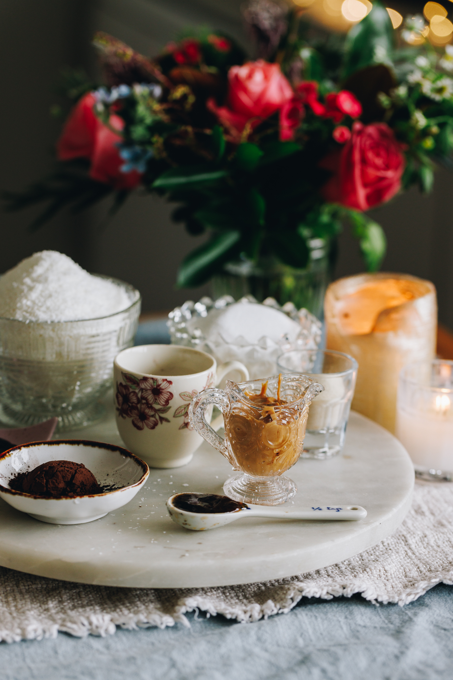 Slice ingredients in vintage jars, on a stone plate with a candle and pink flowers in the background.