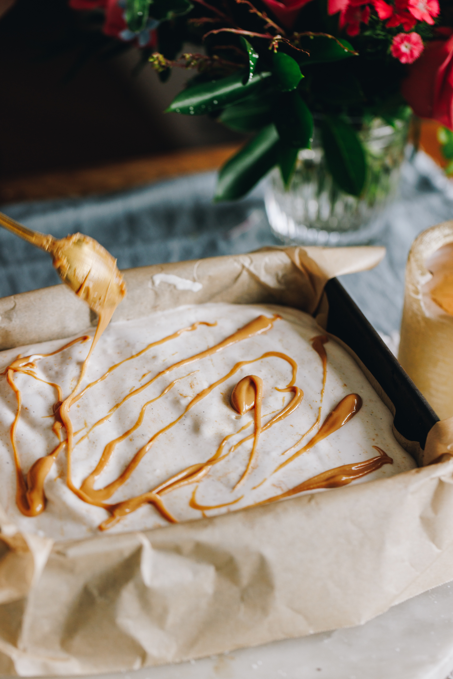 Peanut butter being drizzled on a marshmallow slice, flowers in the background. 