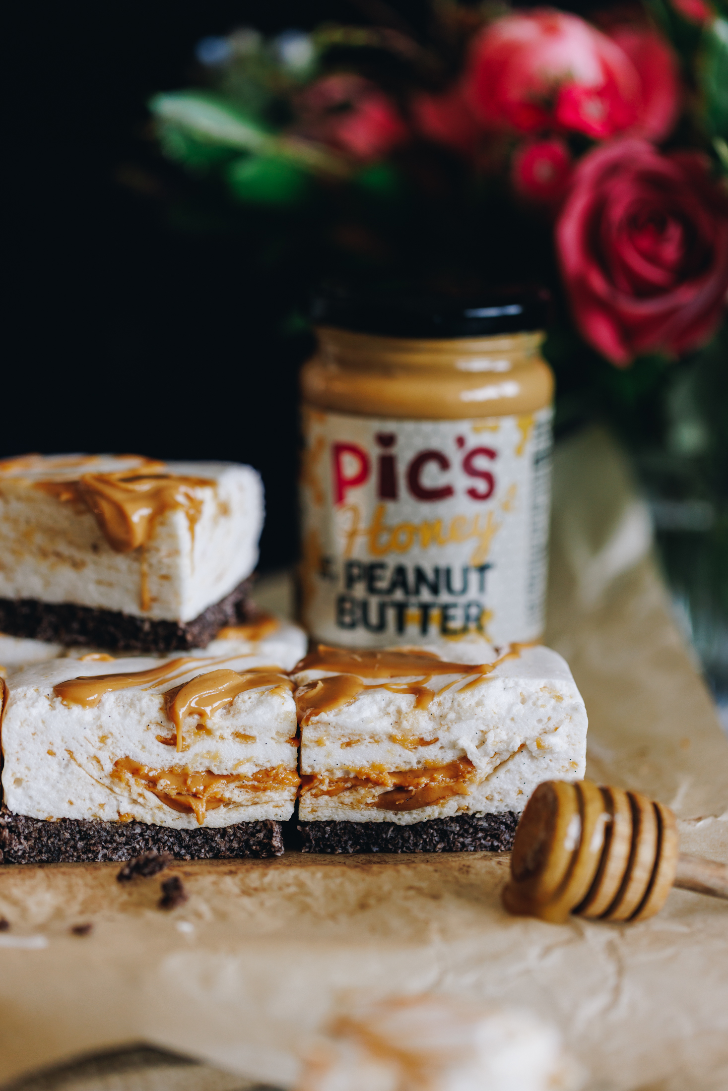 No-bake- peanut butter marshmallow slice on baking paper with Pics honey peanut butter with flowers in the background. 