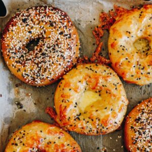 Freshly baked bagels on baking paper with cheese topping and bagel seed mix.