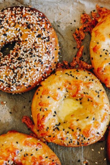 Freshly baked bagels on baking paper with cheese topping and bagel seed mix.