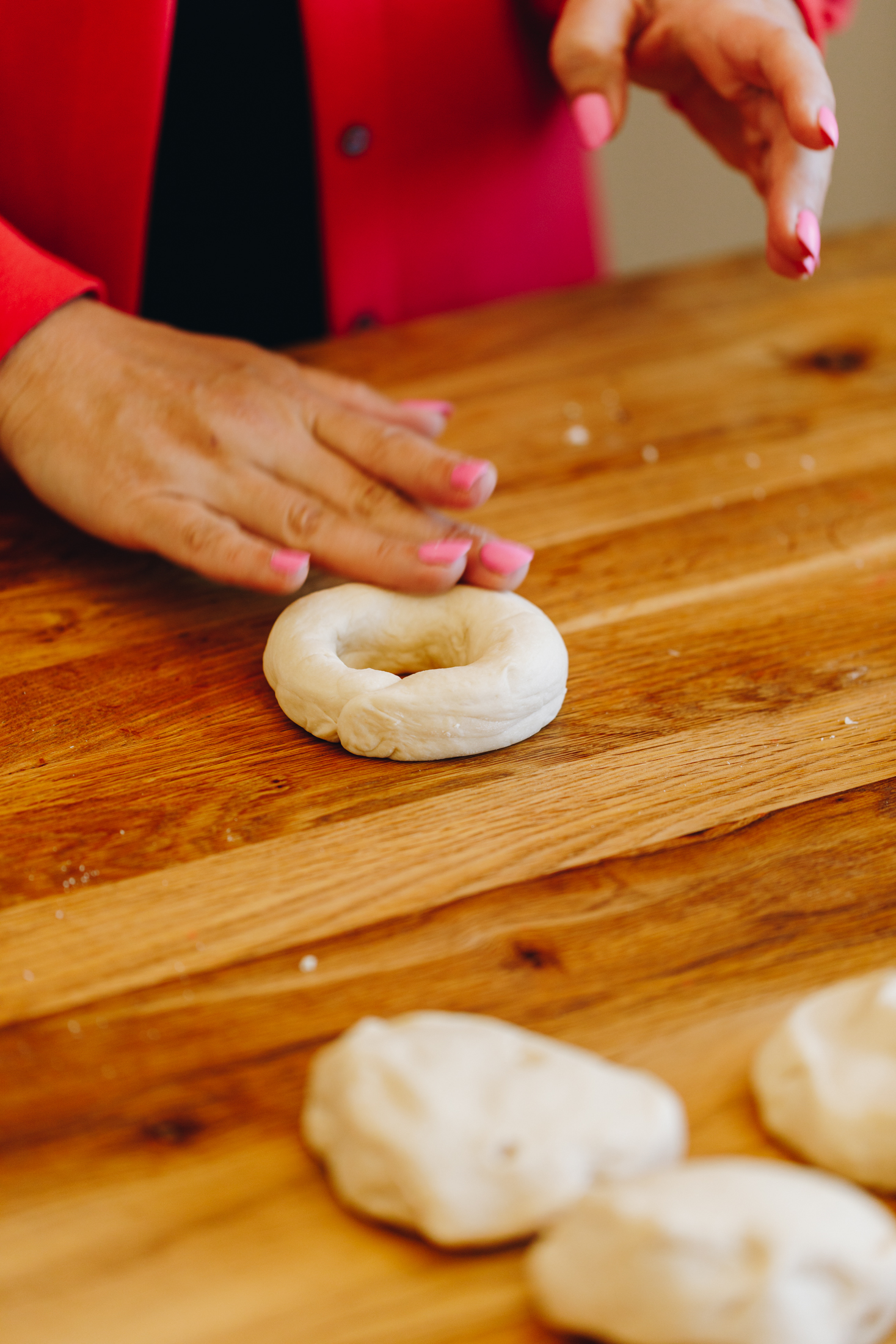 Dough being shaped in to a bagel shape on a wooden table. 